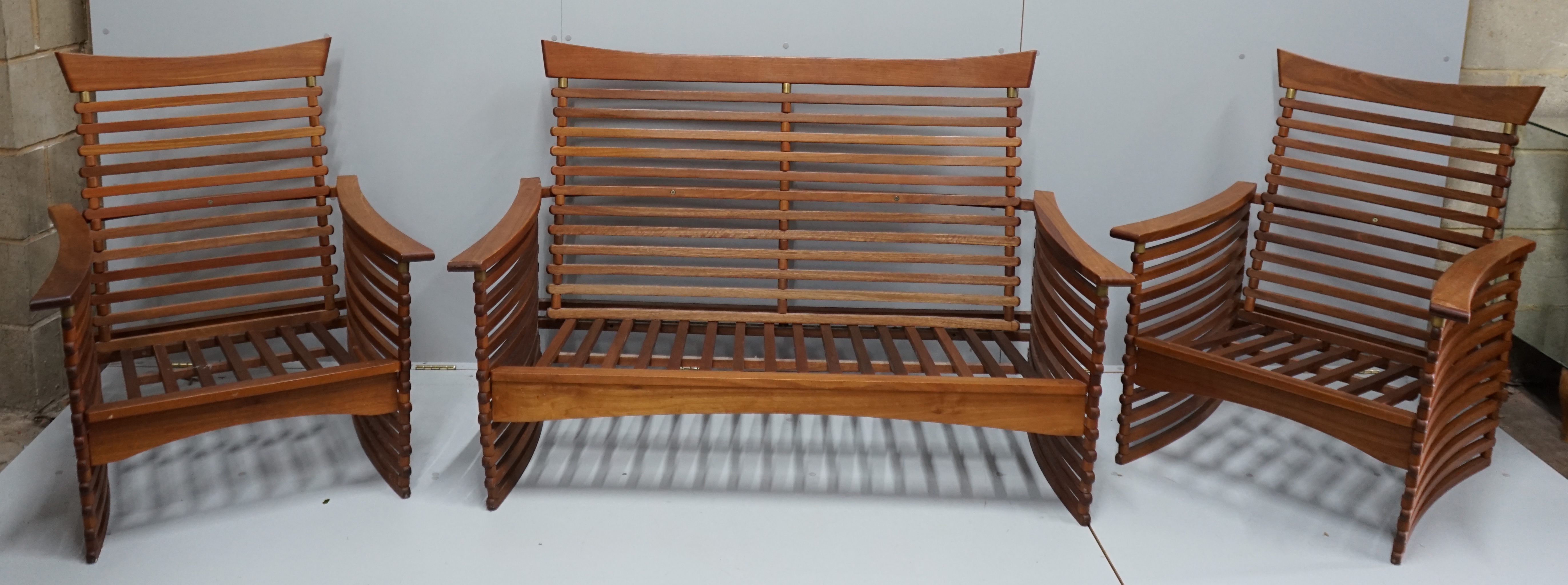 In the manner of Finn Juhl, a Danish brass mounted teak three piece lounge suite of slatted form, settee width 143cm, depth 77cm, height 92cm.
